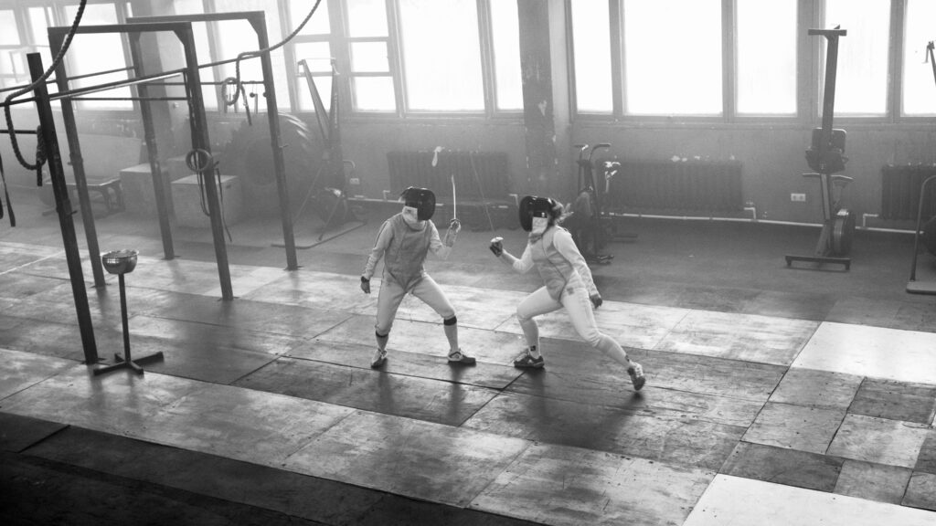 Two fencers in action during a competitive fencing match indoors.